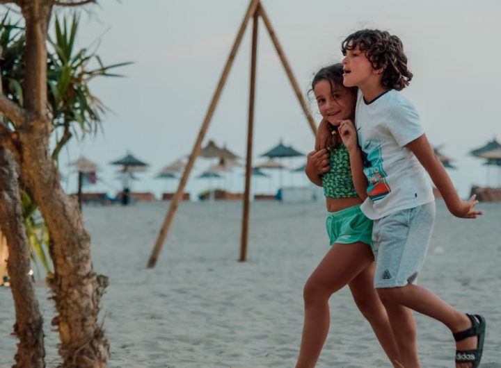 Two children enjoy a playful walk on a sandy beach, capturing summer fun.