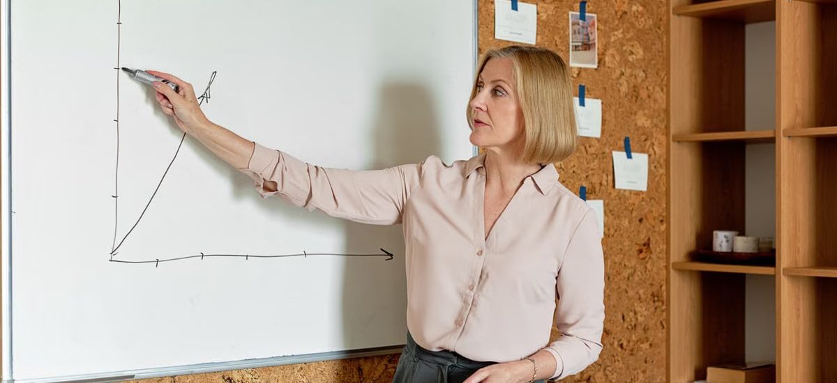 Professional woman explaining data on a whiteboard in a corporate setting.